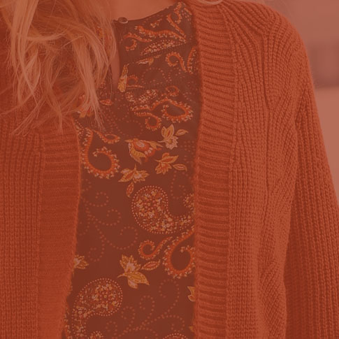 Woman wearing a knit pattern cardigan in rust.